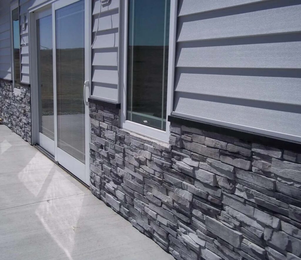 Exterior corner of a modern building featuring a blend of gray stone veneer and sleek horizontal siding, with large glass doors.