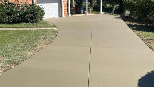 Freshly poured concrete driveway with caution tape, leading to a brick house and a covered porch, surrounded by grassy areas. Freshly poured concrete driveway with caution tape, leading to a brick house and a covered porch, surrounded by grassy areas.