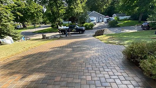 A newly paved brick driveway curves through a landscaped yard, leading to parked cars and homes in a peaceful neighborhood. A newly paved brick driveway curves through a landscaped yard, leading to parked cars and homes in a peaceful neighborhood.