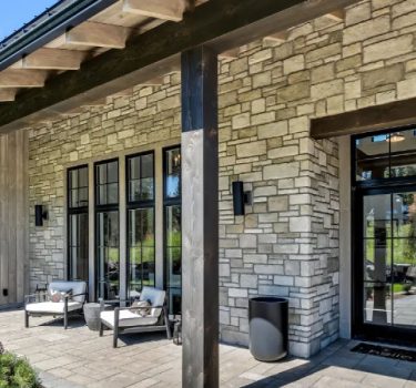 Exterior view of a modern home with stone walls, large windows, and a cozy patio area featuring seating and planters.