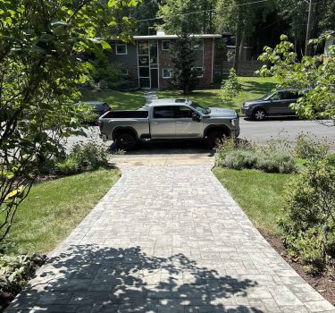 A silver pickup truck parked on a tree-lined street, with a brick house and well-manicured lawn visible in the background.