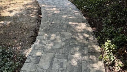 A winding, paved pathway bordered by green grass and low shrubs, with dappled sunlight creating a serene outdoor atmosphere. A winding, paved pathway bordered by green grass and low shrubs, with dappled sunlight creating a serene outdoor atmosphere.